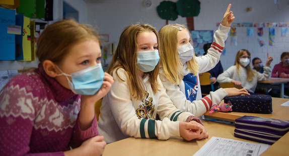 Drei Schüler:innen sitzen mit einer medizinischen Maske im Unterricht.